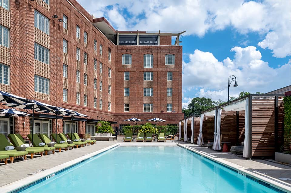 Resort pool with loungers, pergolas, brick building, and tropical landscaping in daylight
