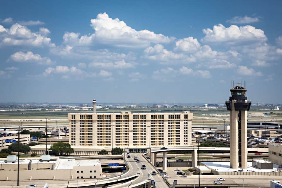 Airport hotel exterior with control tower and runways visible in the background under blue sky