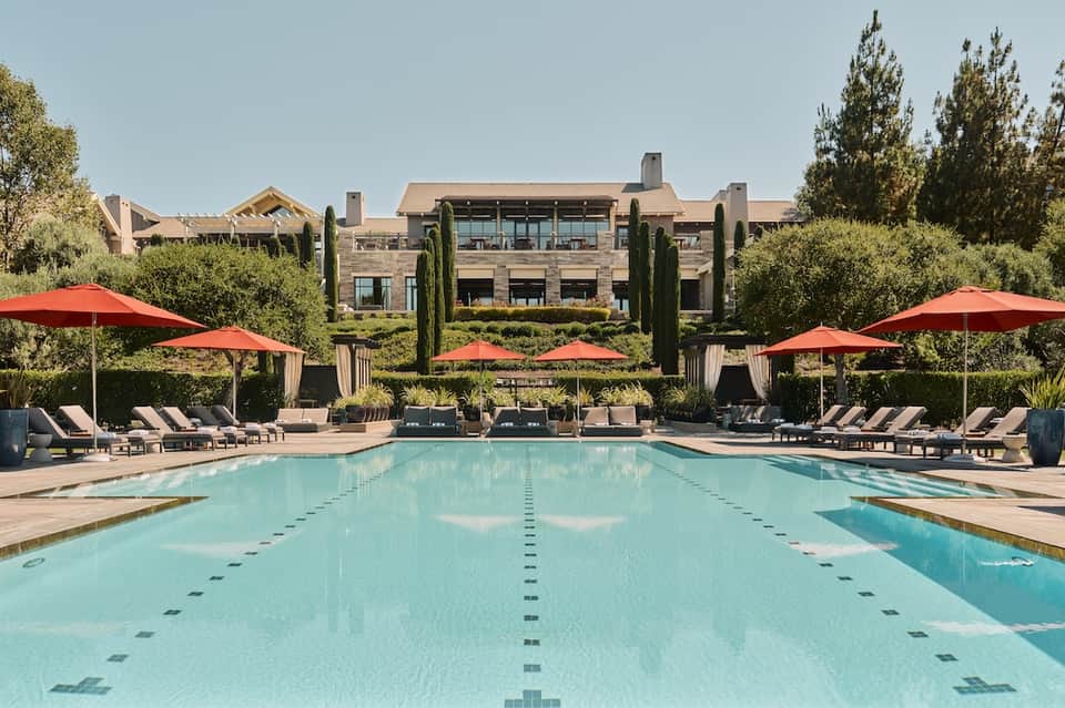 Lap pool with lane dividers, red umbrellas, lounge chairs, and luxury mansion with cypress trees