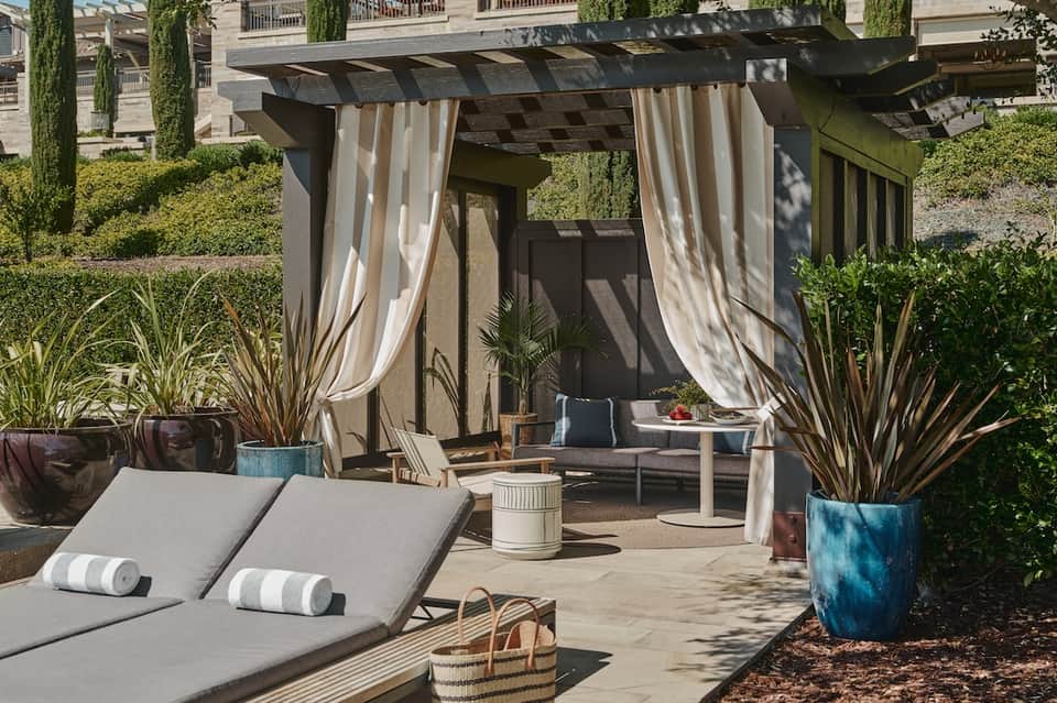 Outdoor patio lounge area with pergola, lounge chairs, striped cushions, and tropical plants