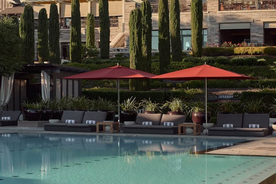 Elegant poolside lounge area with modern furniture, red umbrellas, and cypress trees at luxury resort