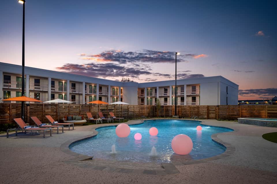 Resort pool at dusk with illuminated pink spheres, loungers, modern apartments, and wooden privacy fence