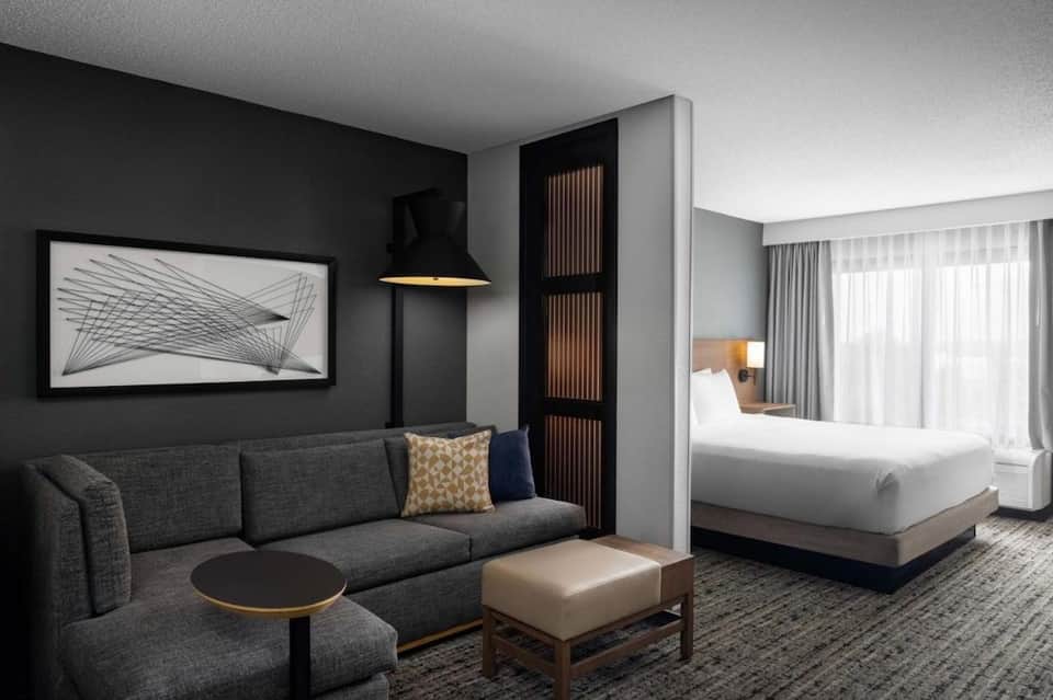 Contemporary hotel suite with dark accent wall, gray sofa, king bed, and minimalist furnishings