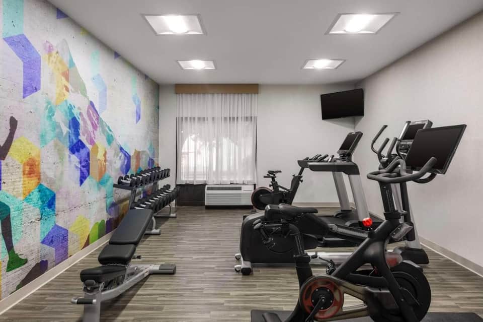Hotel fitness center with cardio equipment, colorful abstract wall mural, and exercise bikes