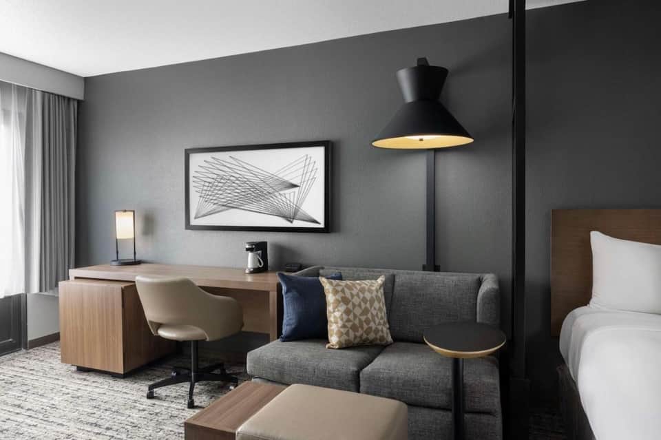 Hotel room with modern gray walls, wooden desk, gray sofa, and pendant lighting