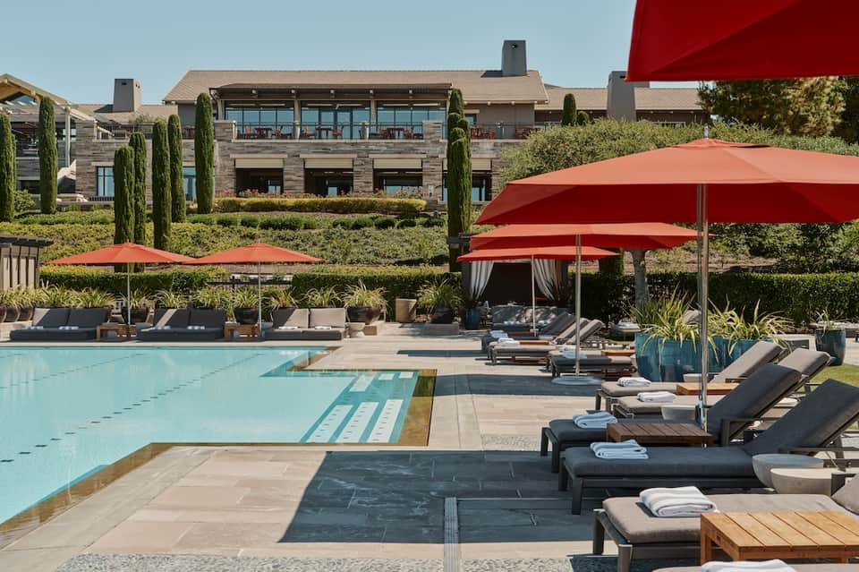 Resort pool with red umbrellas, lounge chairs, stone building, and manicured landscaping