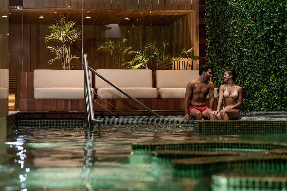 Modern spa pool with wooden lounge chairs, ivy wall, and minimalist design