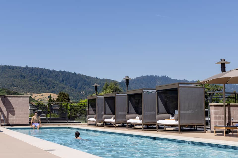 Resort pool with mountainous backdrop, modern cabanas with seating, and guests enjoying the water