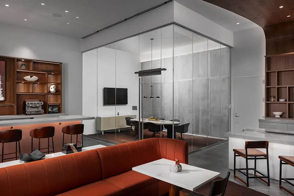 Contemporary office space with glass conference room, red sofa, wood shelving, and pendant lighting