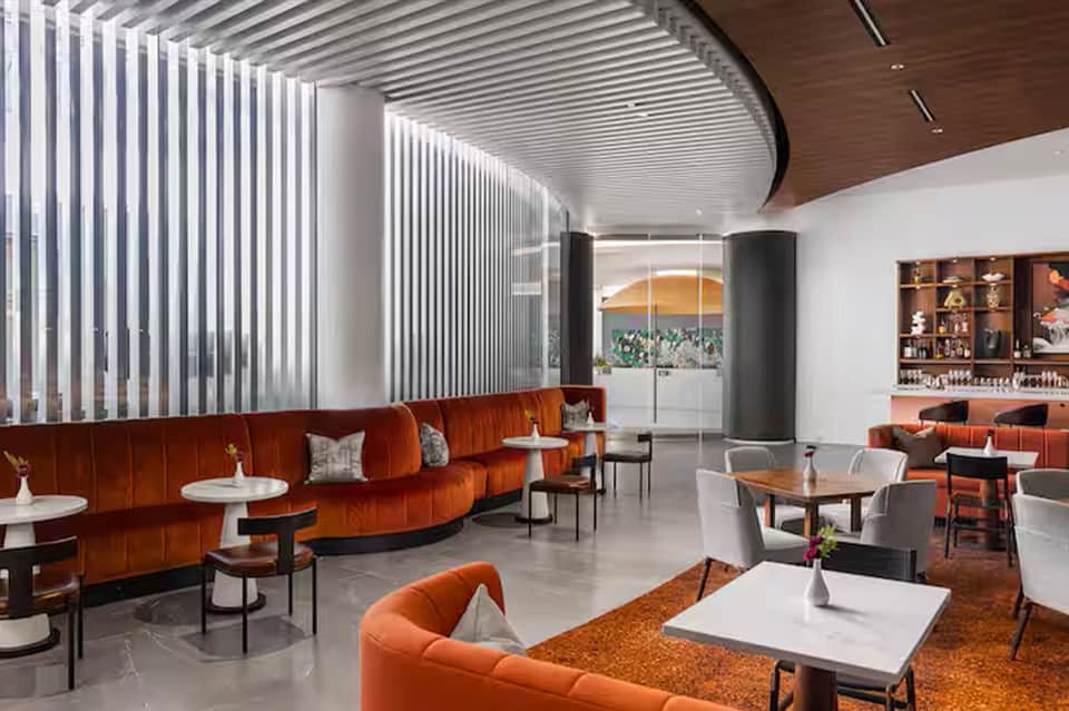 Contemporary hotel lounge with orange seating, vertical blinds, and modern bar area
