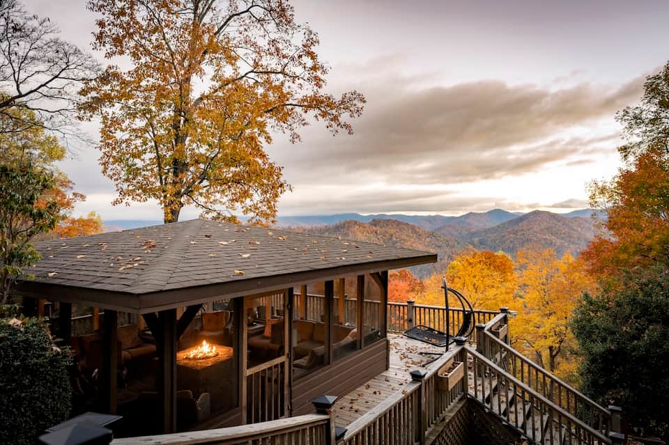 Mountain cabin with fireplace, large windows, and autumn foliage overlooking scenic valley landscape