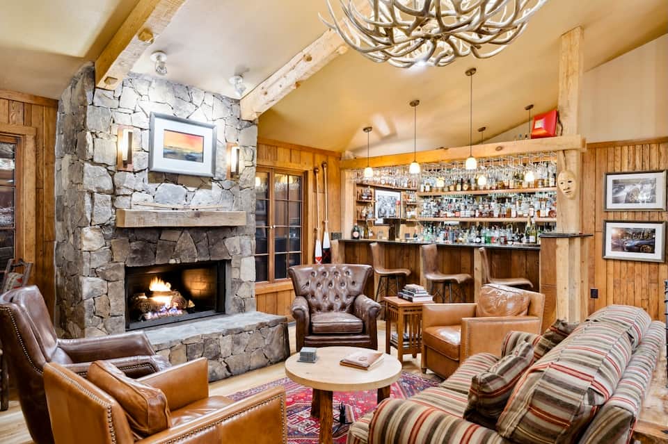 Rustic lodge interior with stone fireplace, wooden bar, leather seating, and warm lighting