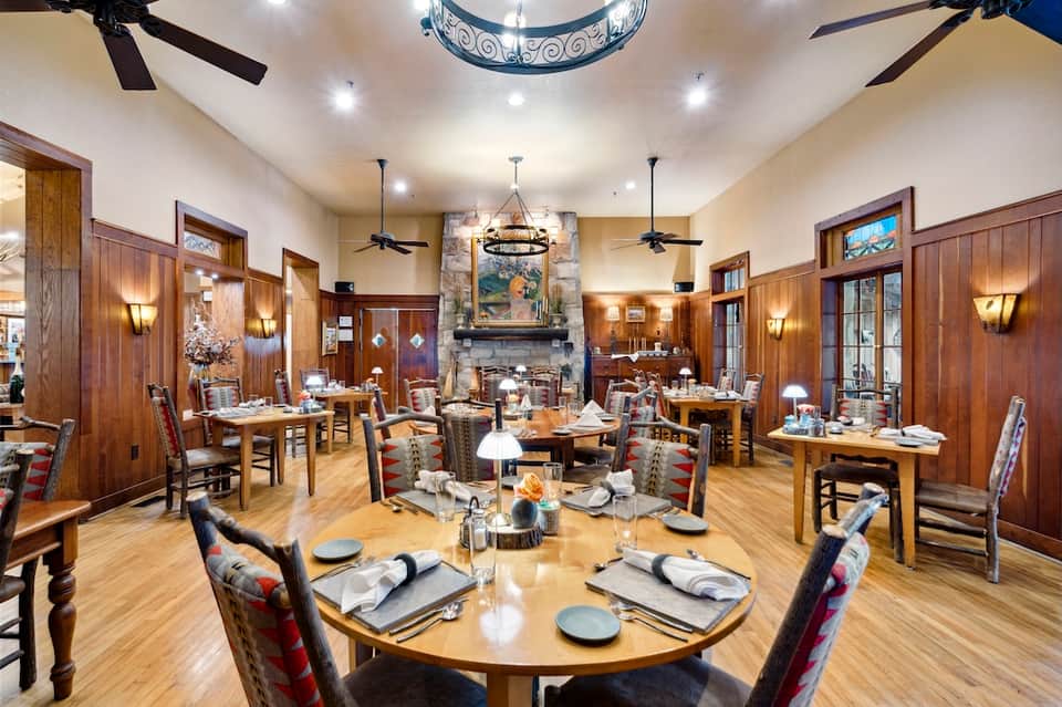 Fine dining restaurant with wooden beams, fireplace, round tables, and rustic elegant decor