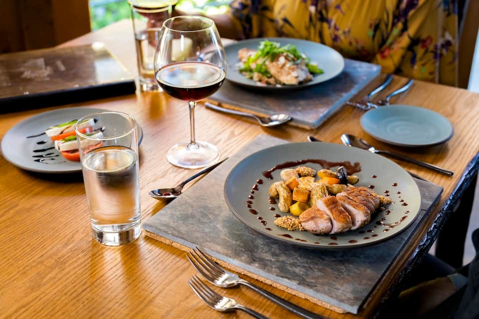 Plated gourmet dinner with duck, roasted vegetables, and wine glasses on wooden table