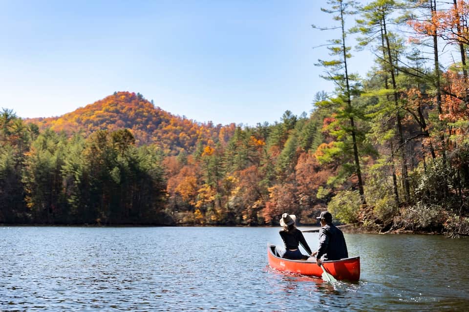 Two people canoeing on calm autumn lake surrounded by forested hills with fall foliage