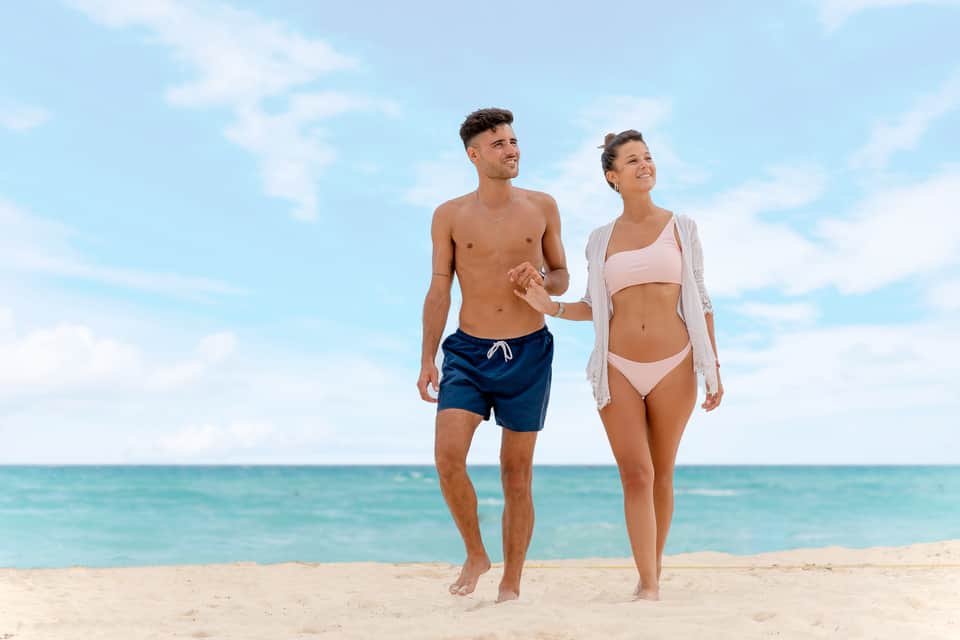 Couple jogging on sandy beach with turquoise ocean and clear blue sky