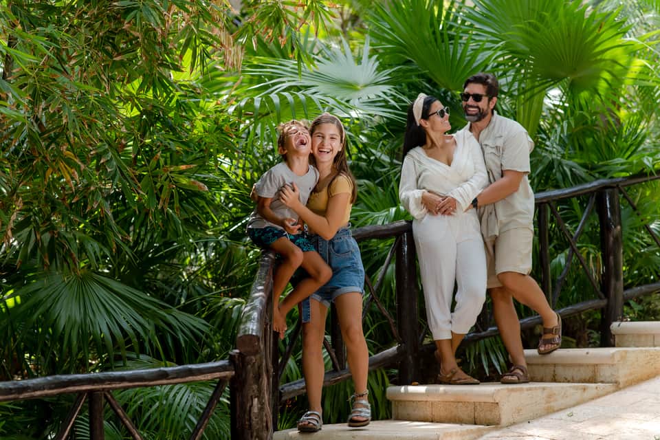 Family of four walking together on a tropical garden pathway with lush green palm vegetation