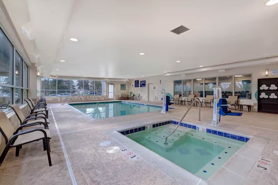 Indoor pool and hot tub facility with large windows and lounge seating area