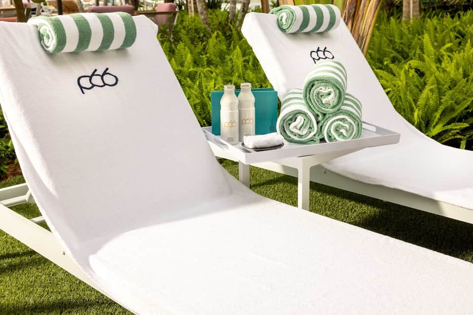 Luxury lounge chairs with branded towels, rolled towels with green stripes, and branded amenity bottles