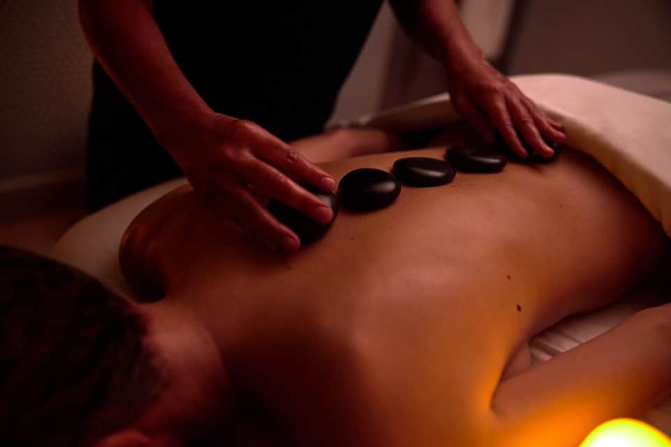 Spa therapist performing hot stone massage on client's back during wellness treatment