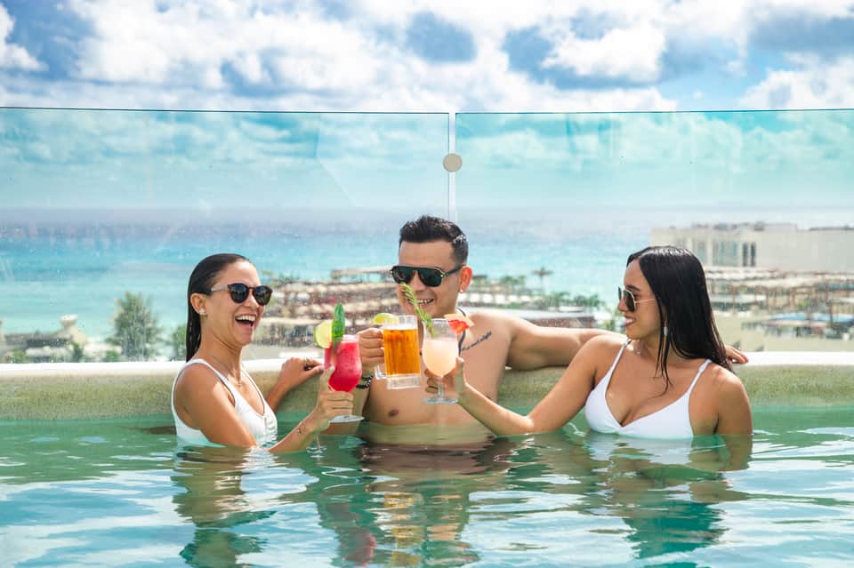 Resort guests enjoying beverages in an infinity pool with ocean and beachfront resort views