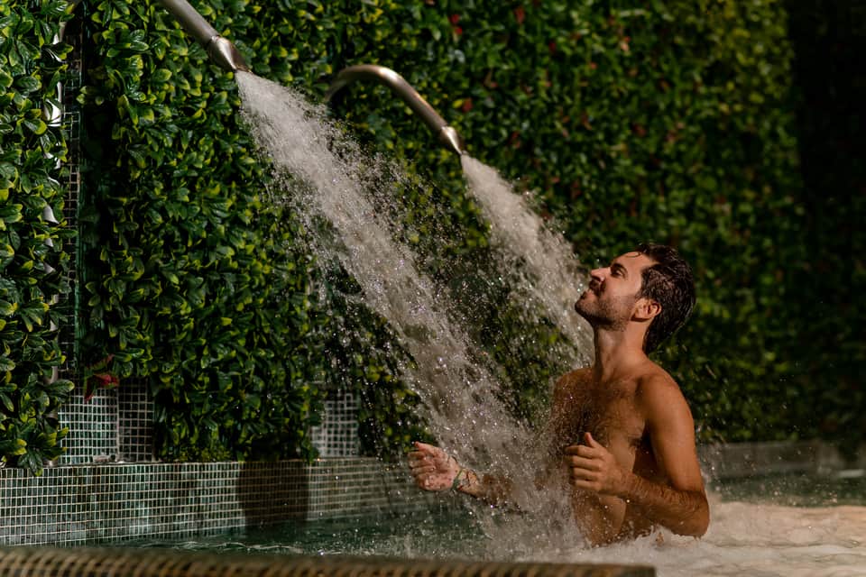 Man enjoying outdoor shower surrounded by lush green ivy walls at tropical resort