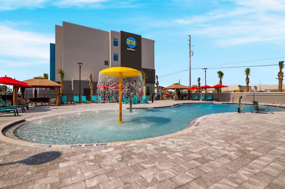 Resort pool with yellow water bucket feature, umbrellas, and hotel building in background
