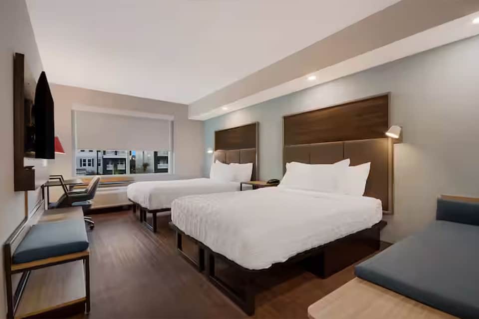 Modern hotel room with two queen beds, brown headboards, desk area, and contemporary furnishings