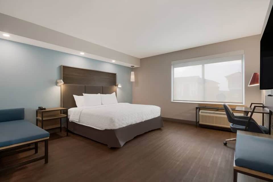 Modern hotel bedroom with dark wood headboard, white bedding, and large windows