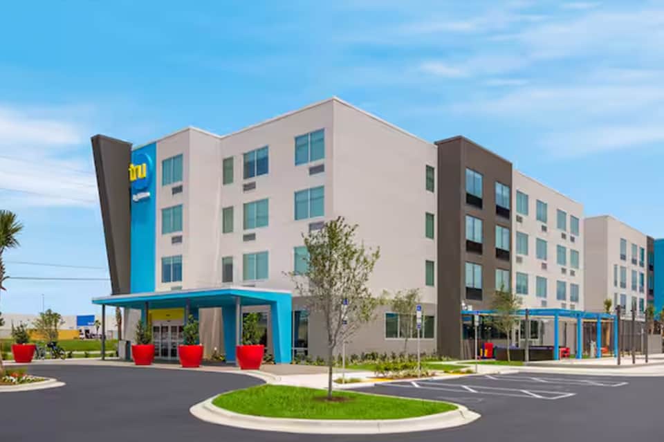 Modern hotel exterior with blue and beige façade, ground-level amenities, and landscaping