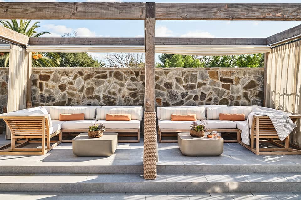 Outdoor seating area with cream cushioned sofas, wooden furniture, and stone accent wall