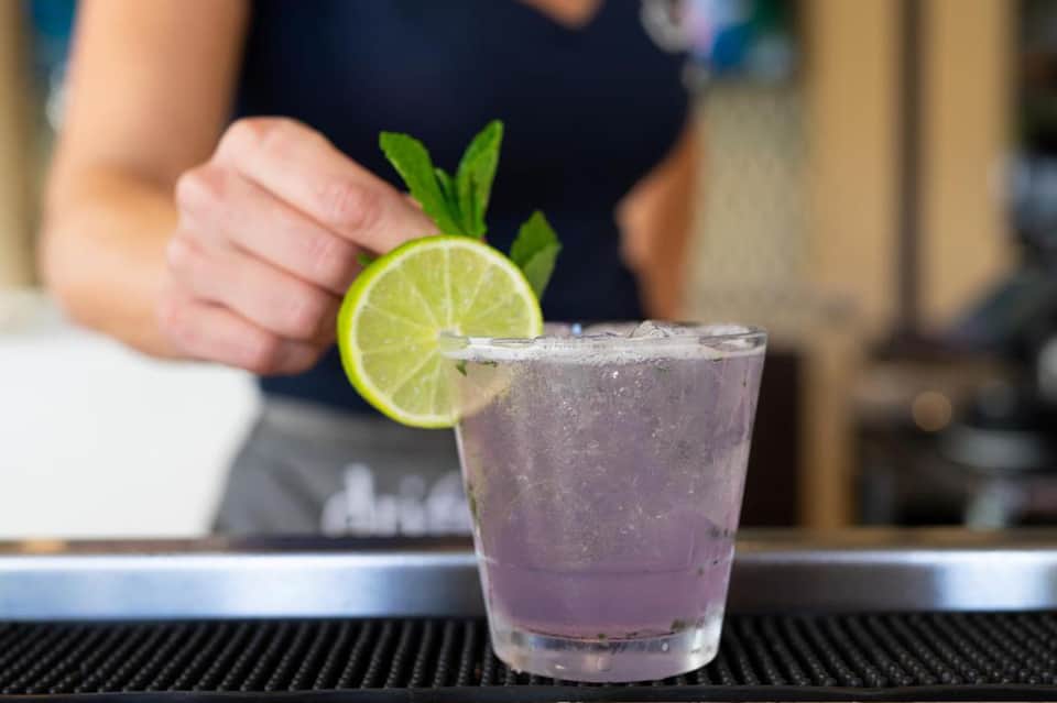 Bartender garnishing cocktail with lime slice and mint on bar counter