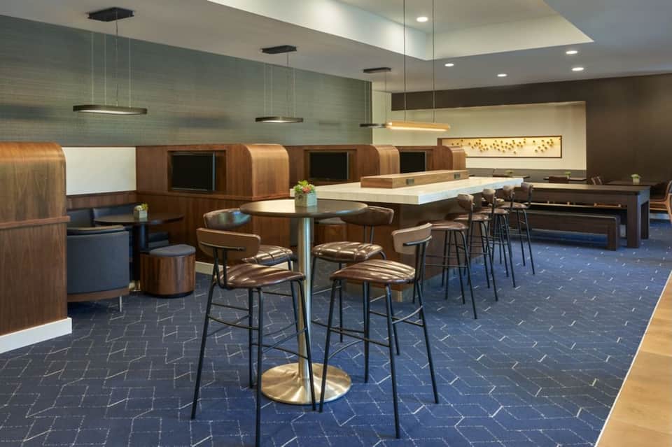 Modern hotel lounge with wooden booth seating, bar counter, and contemporary pendant lighting