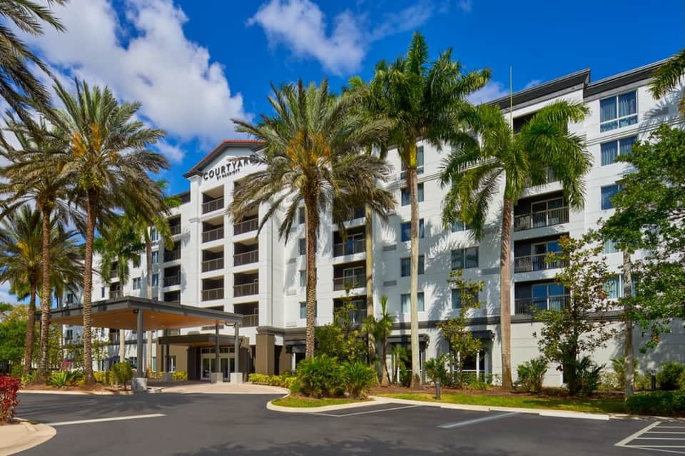 Modern Courtyard hotel exterior with palm trees, white architecture, and covered entrance