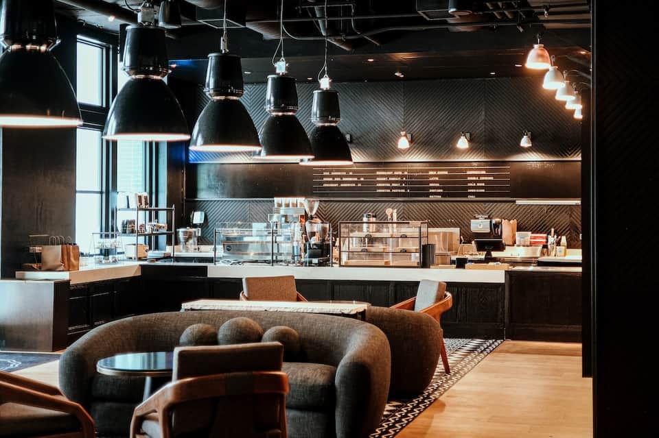 Contemporary hotel café lounge with industrial black pendant lights, curved gray sofa, and modern bar counter