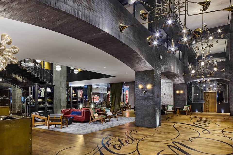 Modern hotel lobby with dramatic lighting, retail shops, red seating, ornate ceiling fixtures, and polished floors