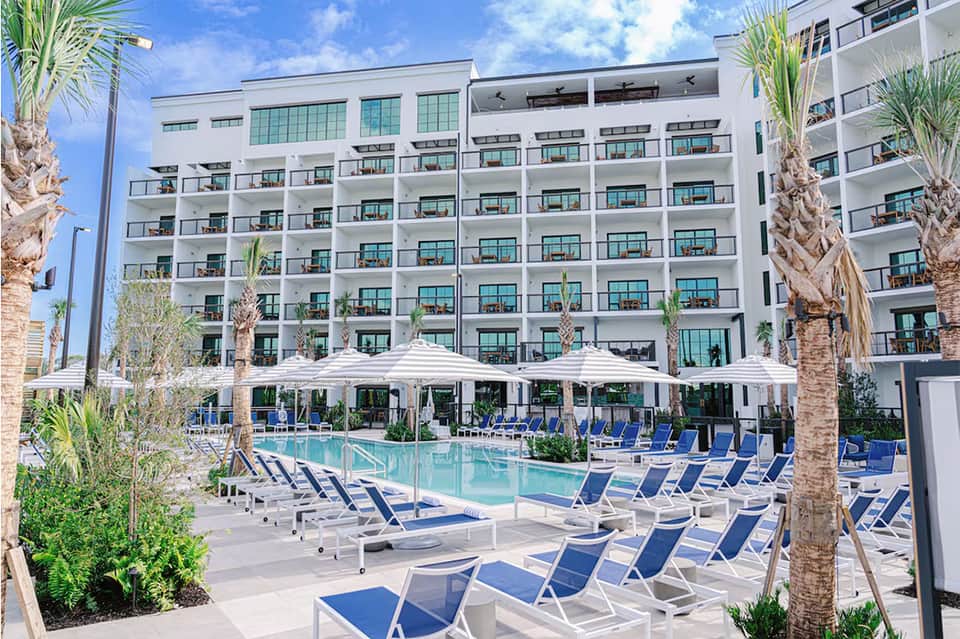 Modern resort pool with blue lounge chairs, white umbrellas, and multi-story hotel building