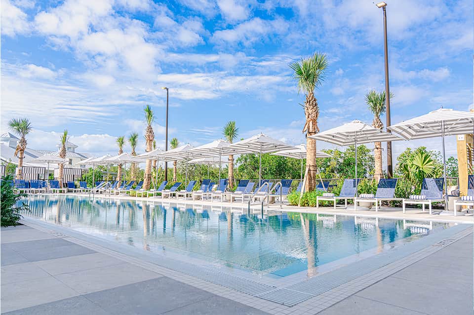 Contemporary resort pool with white umbrellas, palm trees, and loungers reflecting in crystal-clear water