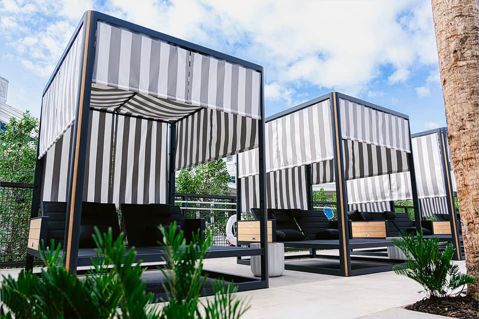 Modern outdoor lounge area with black and white striped shade structures and seating beneath palm trees