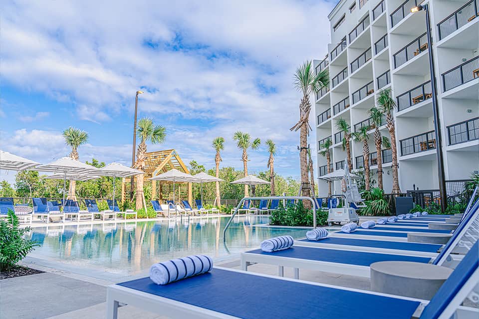 Resort pool deck with blue loungers, pergolas, palm trees, and modern building exterior