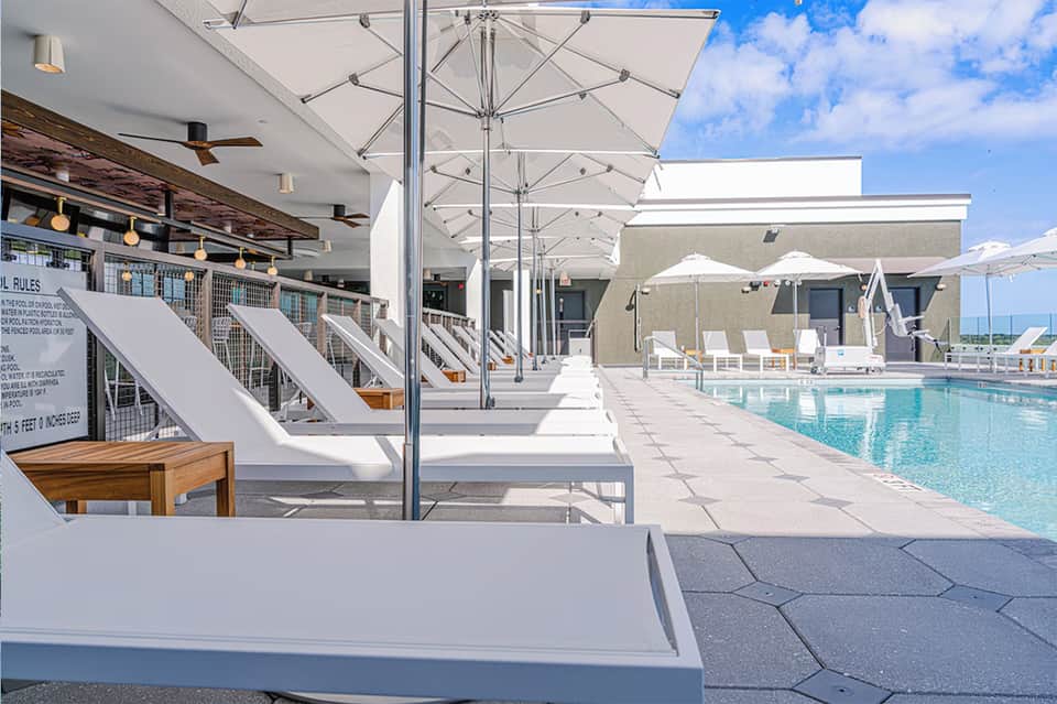 Upscale pool deck with white loungers, umbrellas, lounge chairs, and modern architecture