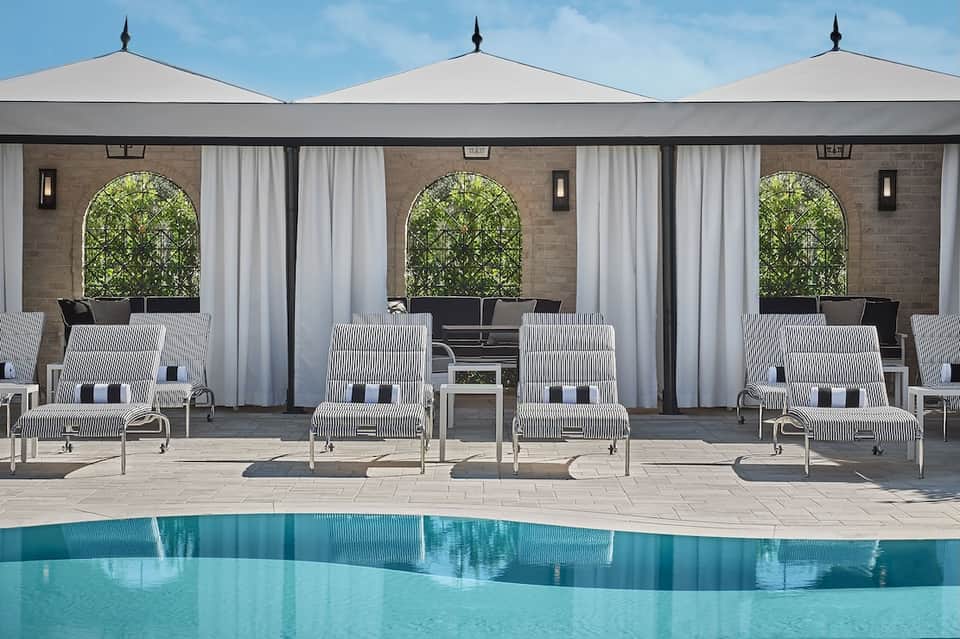 Modern pool cabanas with white umbrellas and striped lounge chairs facing a tranquil blue pool
