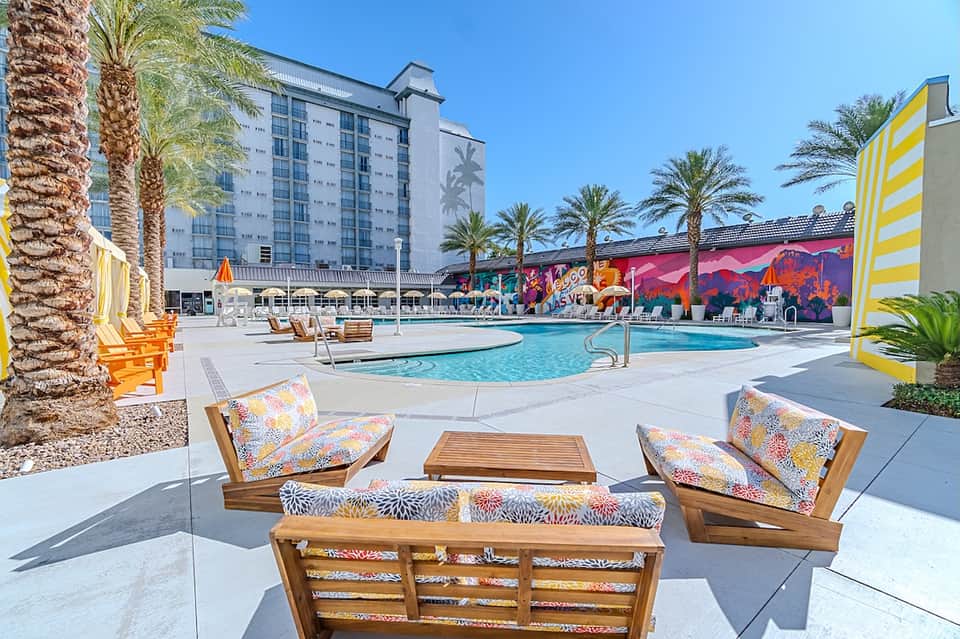 Colorful resort pool with vibrant murals, wooden lounge chairs, and palm trees