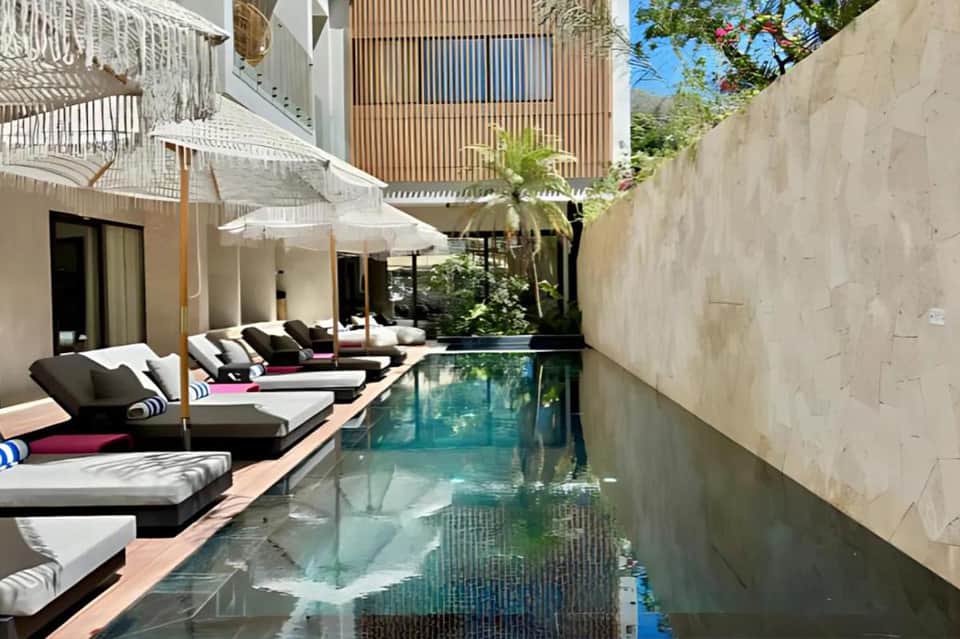 Narrow resort pool with lounge seating, white umbrellas, and multi-story residential building