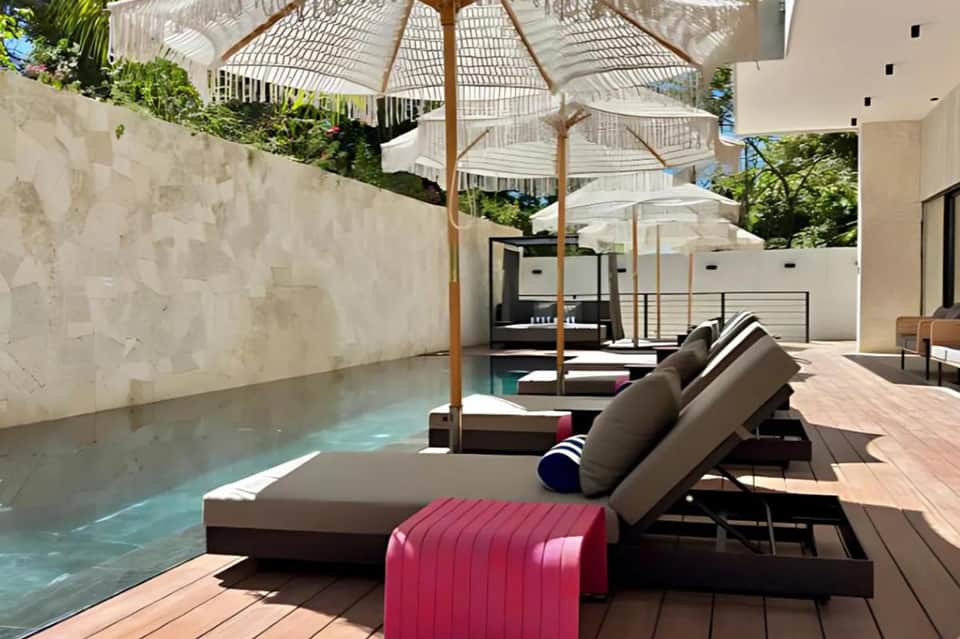 Modern pool terrace with lounge chairs, cream umbrellas, plunge pool, wooden deck flooring