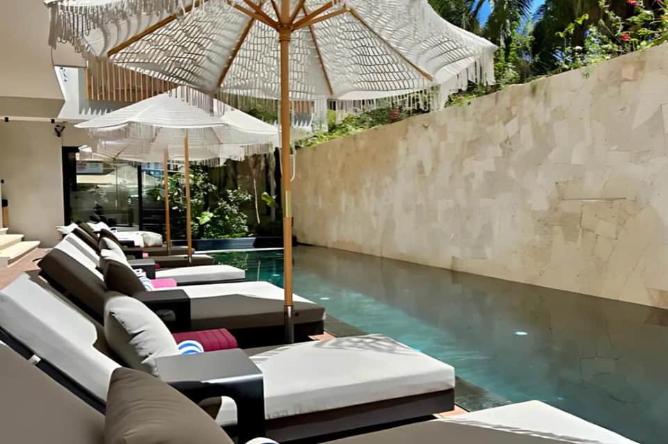 Infinity pool with black lounge chairs, white umbrellas, and modern architecture against stone wall