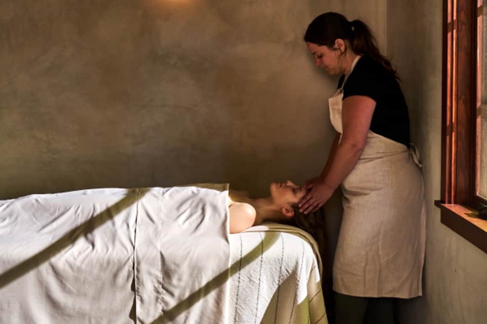 Spa therapist performing massage treatment on client lying on bed in spa room
