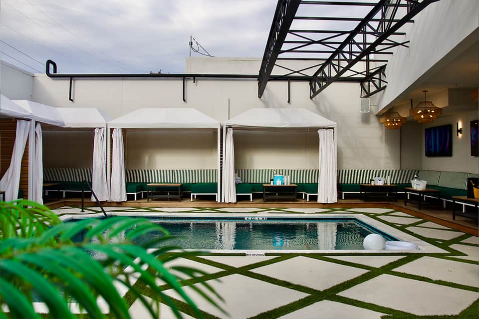 Indoor pool with white cabanas and green loungers under glass roof structure