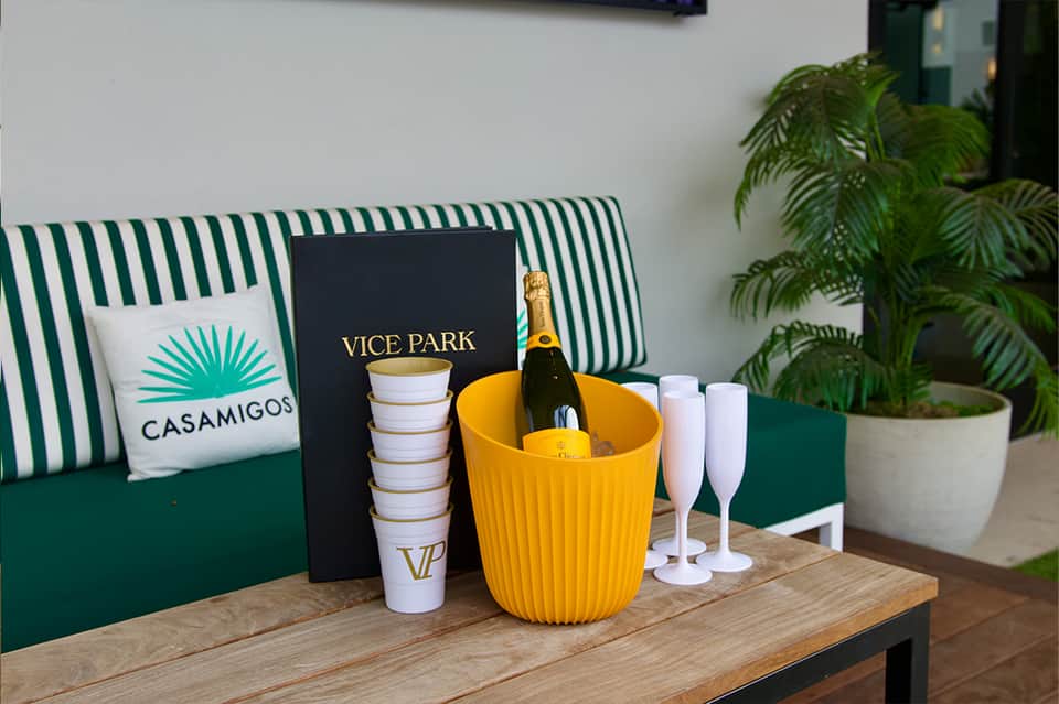 Vice Park branding with champagne bottle in yellow bucket, green striped seating, and palm plant accents