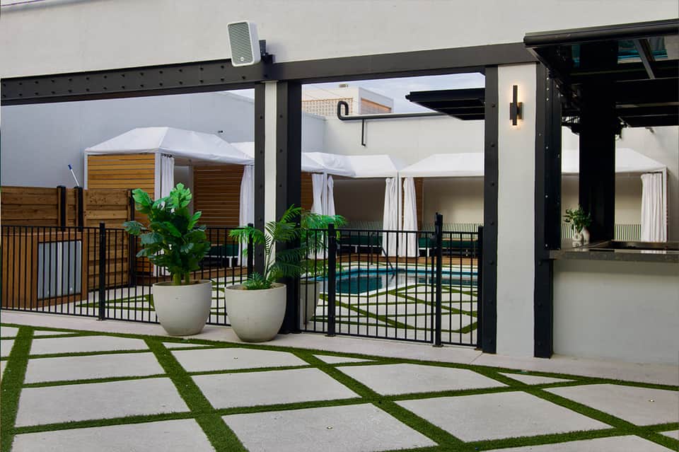Contemporary patio with black steel pergola, white curtains, potted plants, and pool view beyond glass doors